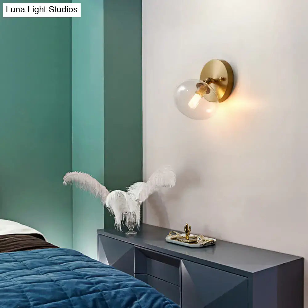 Postmodern brass and glass gold-toned wall sconce with clear globe shade and light bulb included for bedroom lighting