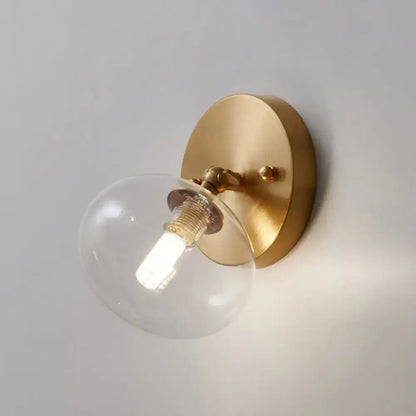 Postmodern brass and glass wall sconce with gold tone clear glass globe and exposed bulb included light type is bedroom lighting