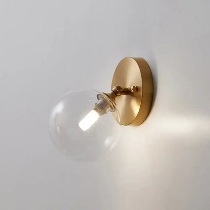 A postmodern brass and glass wall sconce with clear globe housing an illuminated bulb light type bulb included