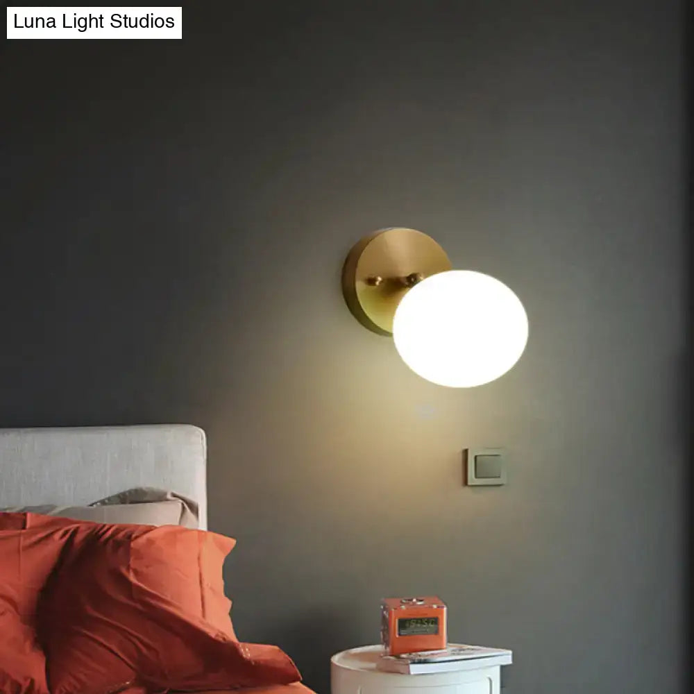 Gold-toned brass and glass postmodern spherical wall sconce with minimalist base and light bulb included for bedroom use