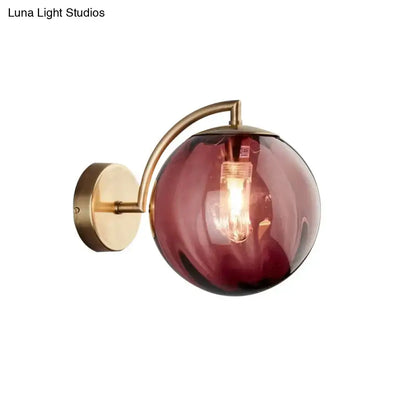 A postmodern brass armed ball sconce with amber glass globe and brass finish ideal for bedroom wall lighting