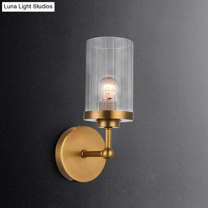 Postmodern brass cylinder wall light with clear vertically ribbed glass and exposed bulb for bedroom use