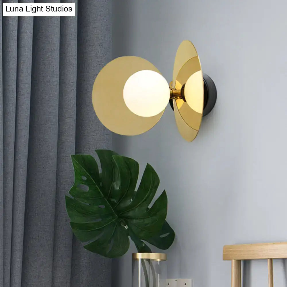 Gold-toned postmodern brass mini milk glass wall light with circular frosted bulb and overlapping disc shades for bedroom