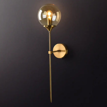 Postmodern brass pencil arm wall lamp with gold-toned stem and spherical amber glass shade for bedroom sconce use