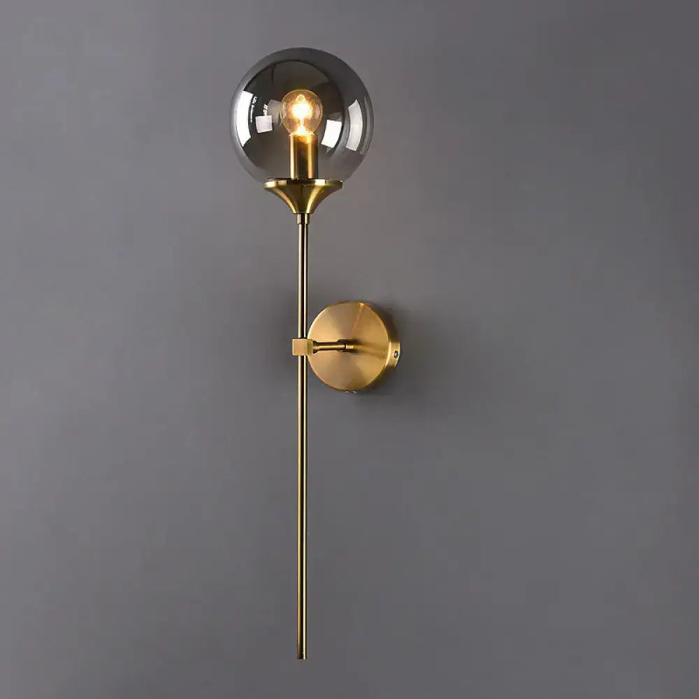 Postmodern brass pencil arm wall lamp with gold-toned finish, smoked glass globe, and exposed filament bulb for bedroom sconce