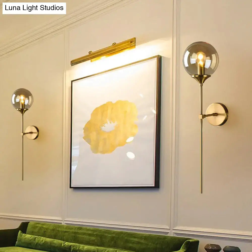 Gold-toned spherical globe wall lamp with brass pencil arm, slender stem, and circular wall plate for bedroom sconce