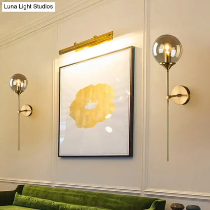 Gold-toned spherical globe wall lamp with brass pencil arm, slender stem, and circular wall plate for bedroom sconce