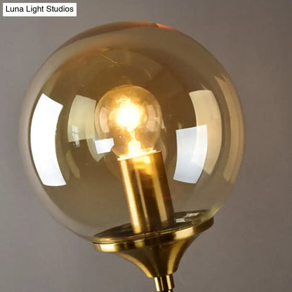 Postmodern brass pencil arm wall lamp with amber glass shade and illuminated filament bulb for bedroom sconce lighting