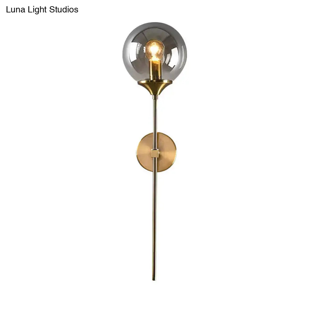Postmodern brass pencil arm wall lamp with smoked glass globe and brass-finished metal stem for bedroom sconce use