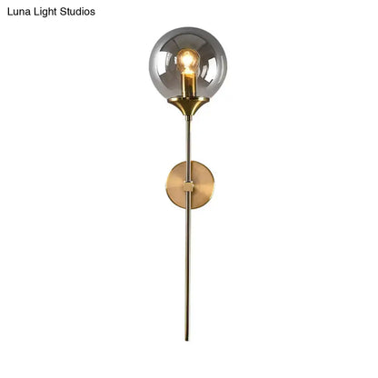 Postmodern brass pencil arm wall lamp with smoked glass globe and brass-finished metal stem for bedroom sconce use