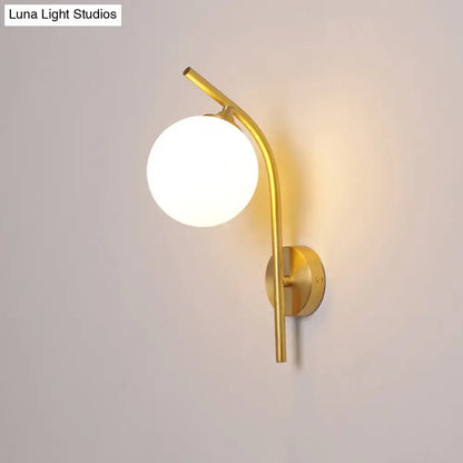 Postmodern brass wall sconce with a gold-toned curved arm and white glass geometric frosted globe shade for living room