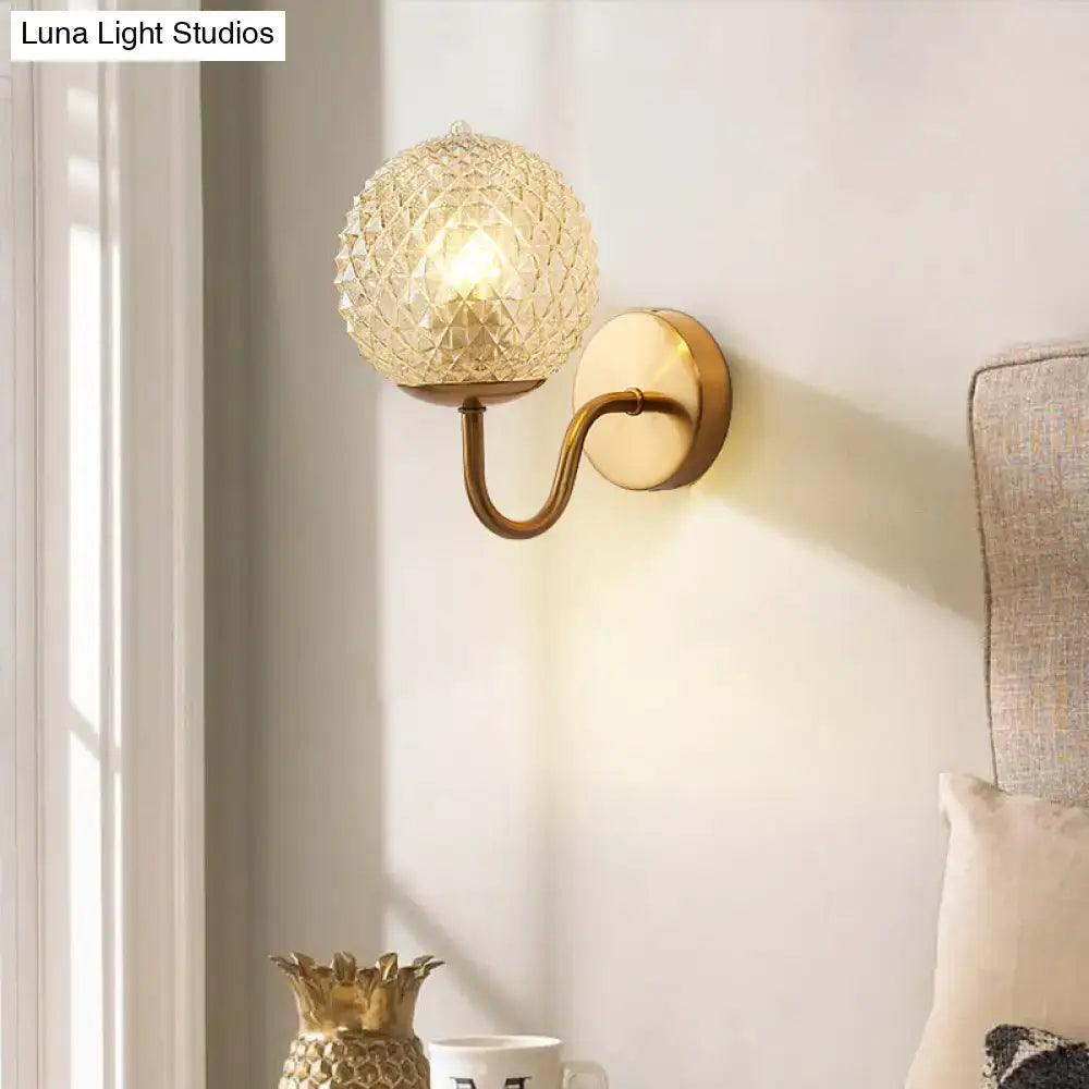 A warm-toned brass postmodern wall sconce with a gold ball shaped textured glass shade for bedroom lighting