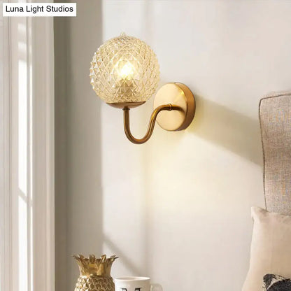 A warm-toned brass postmodern wall sconce with a gold ball shaped textured glass shade for bedroom lighting