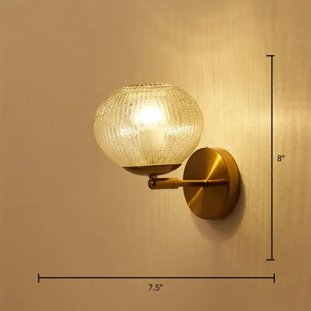 Brass-finished postmodern ball shaped wall sconce with textured glass shade for bedroom lighting