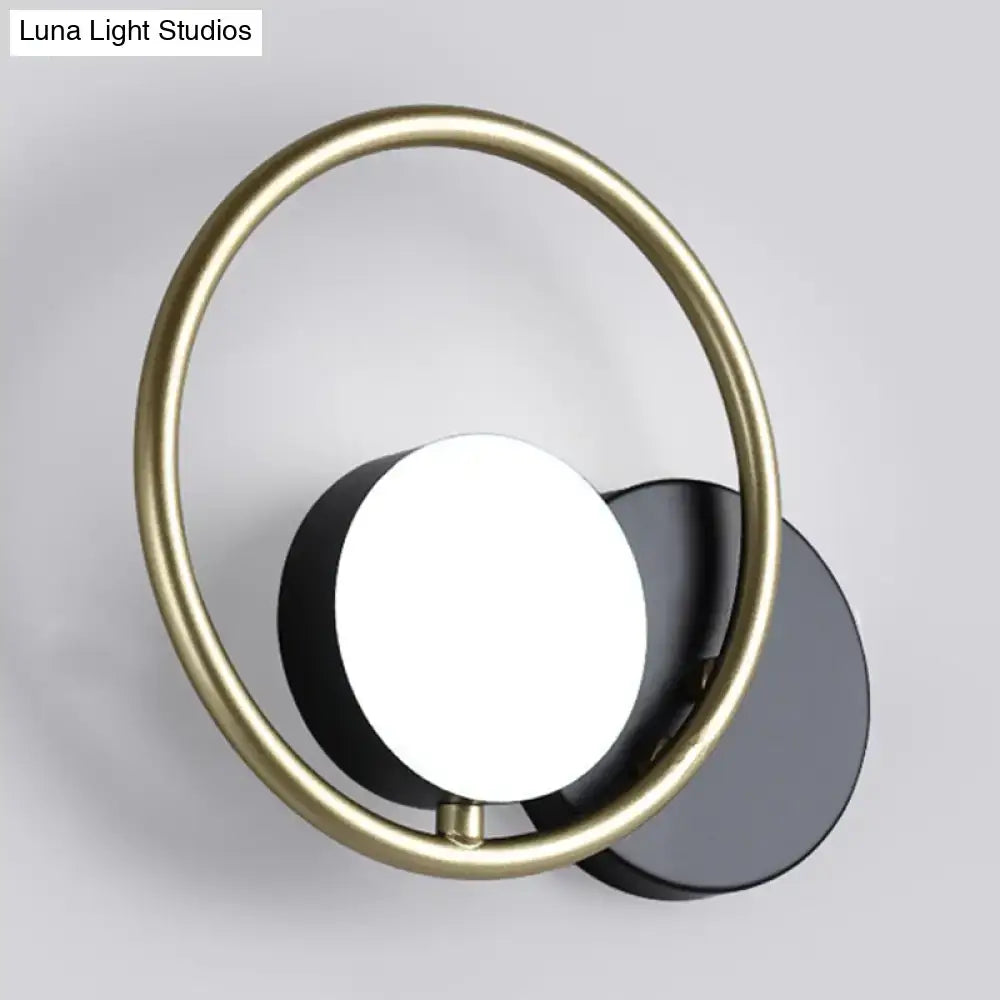 Modern wall mounted light with a gold-toned circular frame black matte accents and a white illuminated disc ring design