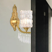 Postmodern gold column wall lamp with ornate design, faceted crystal shade, and dangling teardrop crystals for bedroom lighting