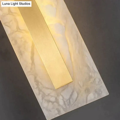 Modern wall lamp featuring a polished brass center with warm light and a white gray copper marble wall backplate