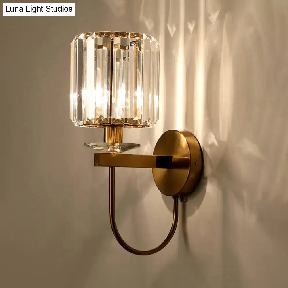 DecorBites™ postmodern gold cylindrical crystal wall sconce with curved arm and brass-finished metal base with warm light