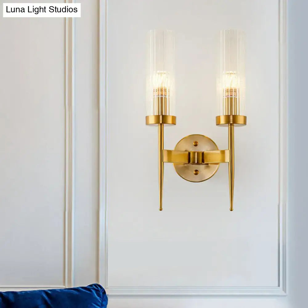 Postmodern gold-toned wall sconce with two slender arms featuring clear ribbed glass cylinders and exposed filament bulbs