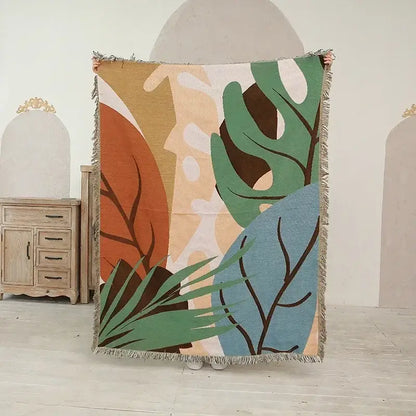 A woven ethnic tapestry sofa blanket with abstract botanical design in olive pink tones and fringed edges for living room