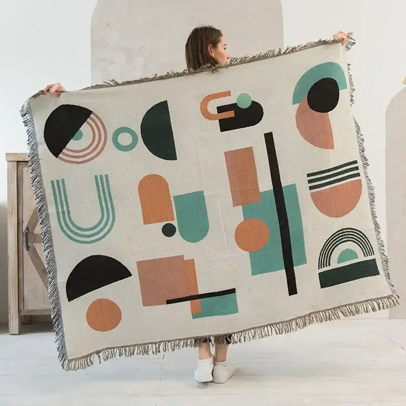 A cream ethnic tapestry sofa blanket with a modern geometric pattern in teal black and terracotta and fringed edges
