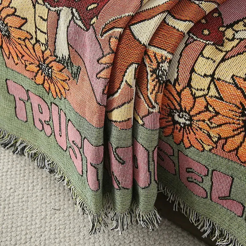 A vibrant ethnic tapestry sofa blanket in olive pink with floral patterns and trust lettering on woven fabric