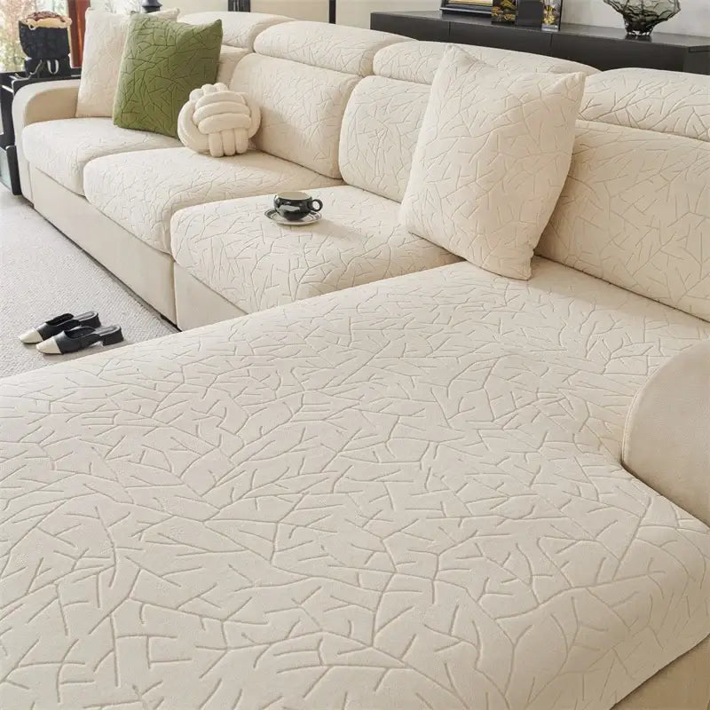 Cream-colored quilted sofa cover with subtle leaf pattern made of elastic fabric for living room use