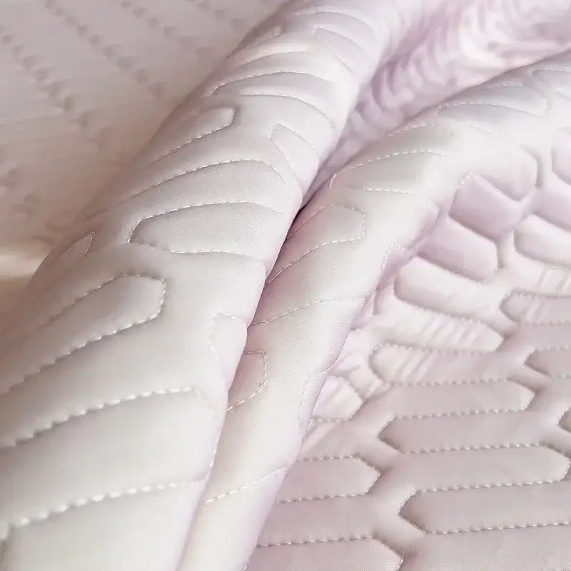 Quilted pink bed skirt set with silver trim featuring soft white fabric with lavender hue and geometric stitching patterns
