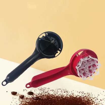 Red and black plastic espresso coffee machine brush cleaning tool with perforated heads and scattered ground beans nearby