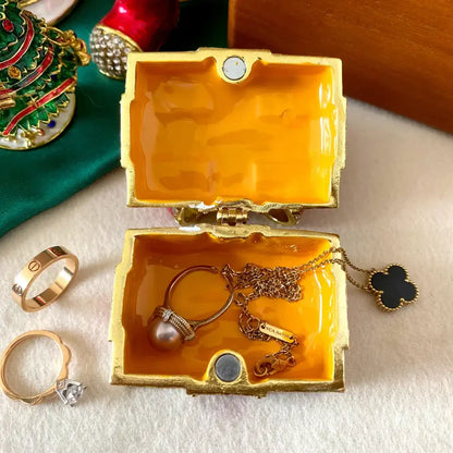 Gold-trimmed red and white bow jewelry trinket box with vibrant orange interior holding delicate pearl ring and pendant