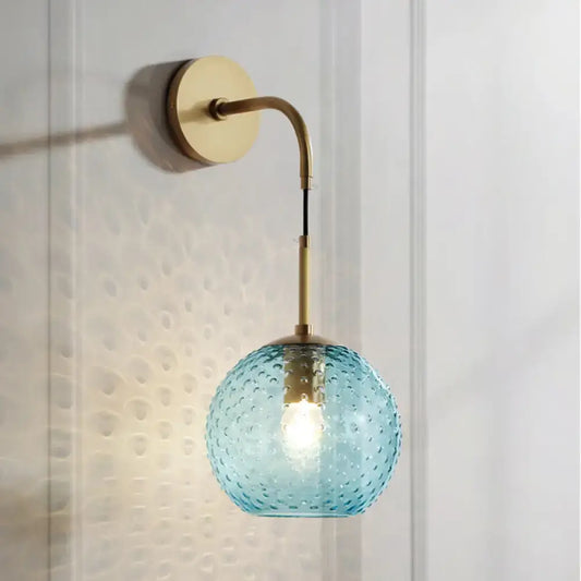 Retro blue glass globe wall lamp with textured light blue glass and brass accents featuring pink yellow blue hues