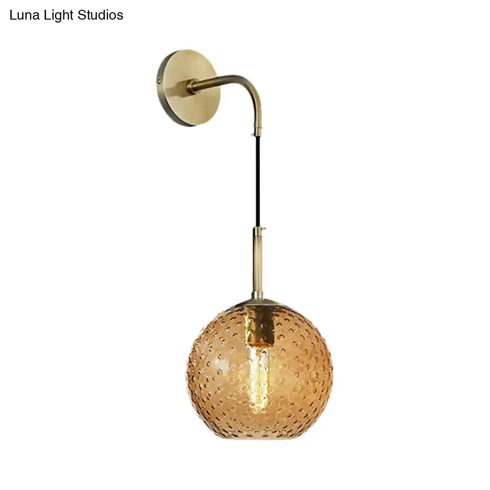 A warm amber glass globe sconce with textured bubble surface and brass hardware for pink yellow blue retro lighting