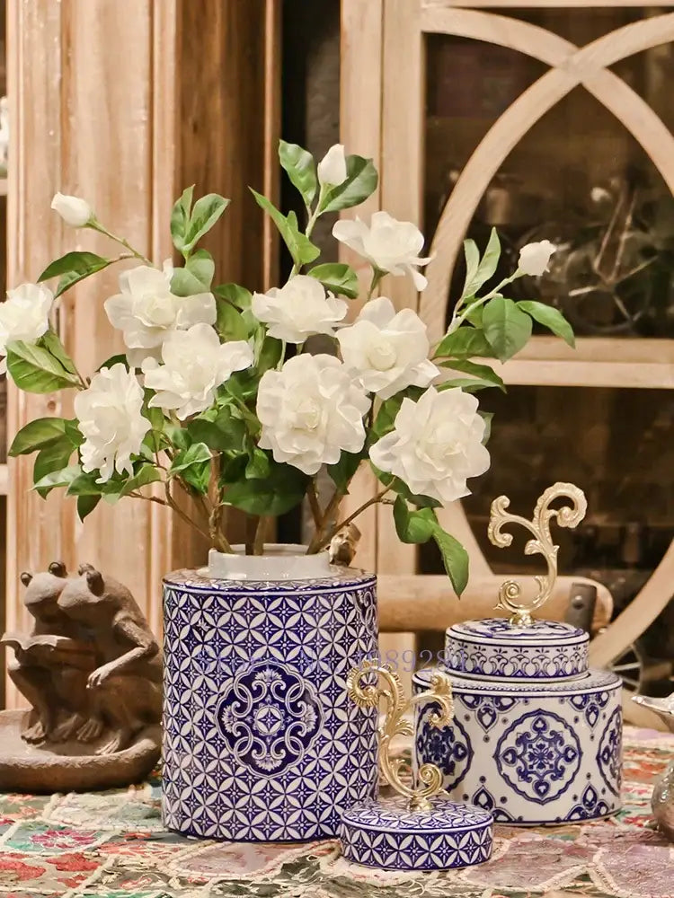 Retro blue and white porcelain covered vase jar with ornate gold accents holding artificial white flowers for living room storage