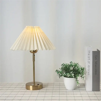 Cream-colored pleated table lamp with brass-finished base and stem featuring an adjustable pleated design for bedroom use