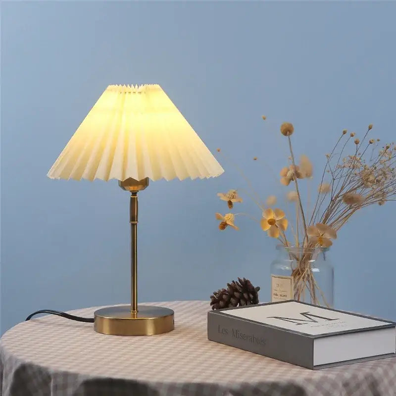A warm-toned brass decorbites adjustable pleated table lamp with a cream fabric shade for bedroom lighting