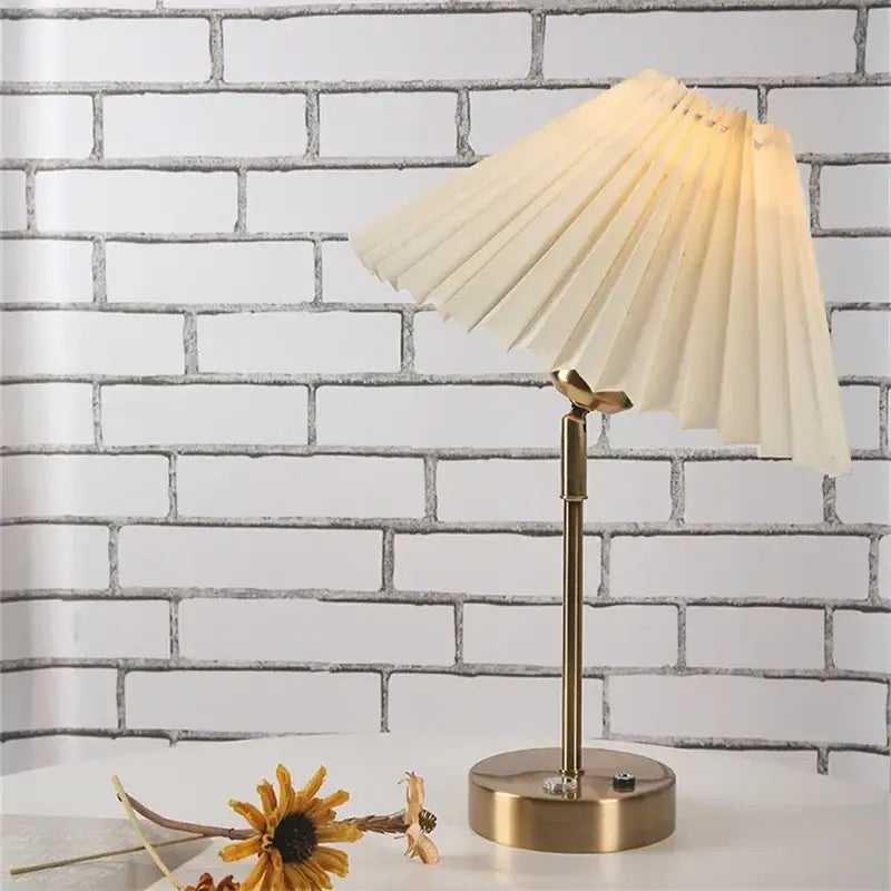 A cream-colored pleated fabric lampshade on a brass-finished decorbites adjustable pleated table lamp stand