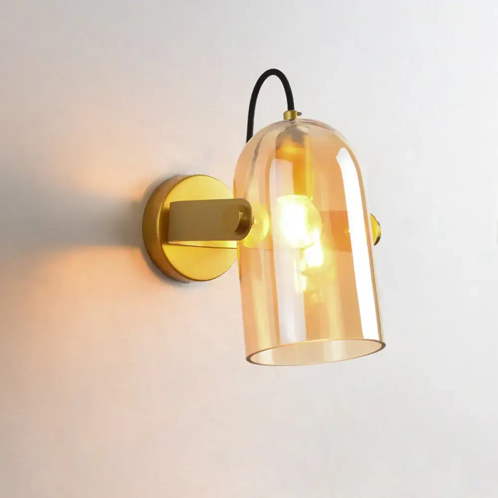 A warm amber glass bell-shaped cloche sconce light with gold metal base and black cord ideal for bedroom use
