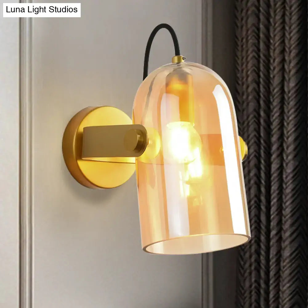 Warm amber glass bell-shaped sconce light with brass finish and black cord complements retro cloche sconce light design