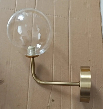 A sleek retro brass wall lamp with a curved arm and clear decorbites glass ball for bedroom lighting