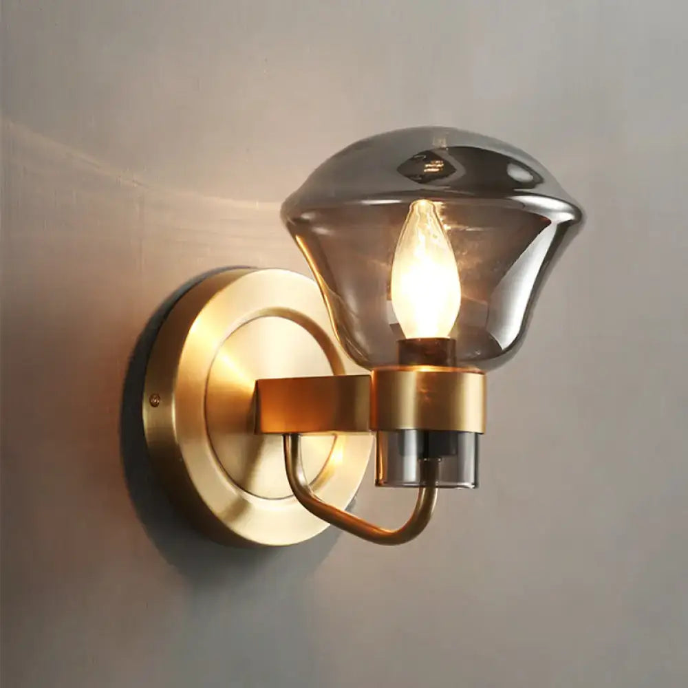 A sleek brass light fixture with smoke gray amber glass shade and exposed filament bulb for bedroom sconce lighting