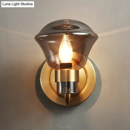 A warm-toned brass light fixture with smoke gray amber glass shade and exposed filament bulb for bedroom sconce