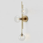 Retro brass wall sconce with three clear glass globe bulbs arranged vertically for dining room lighting