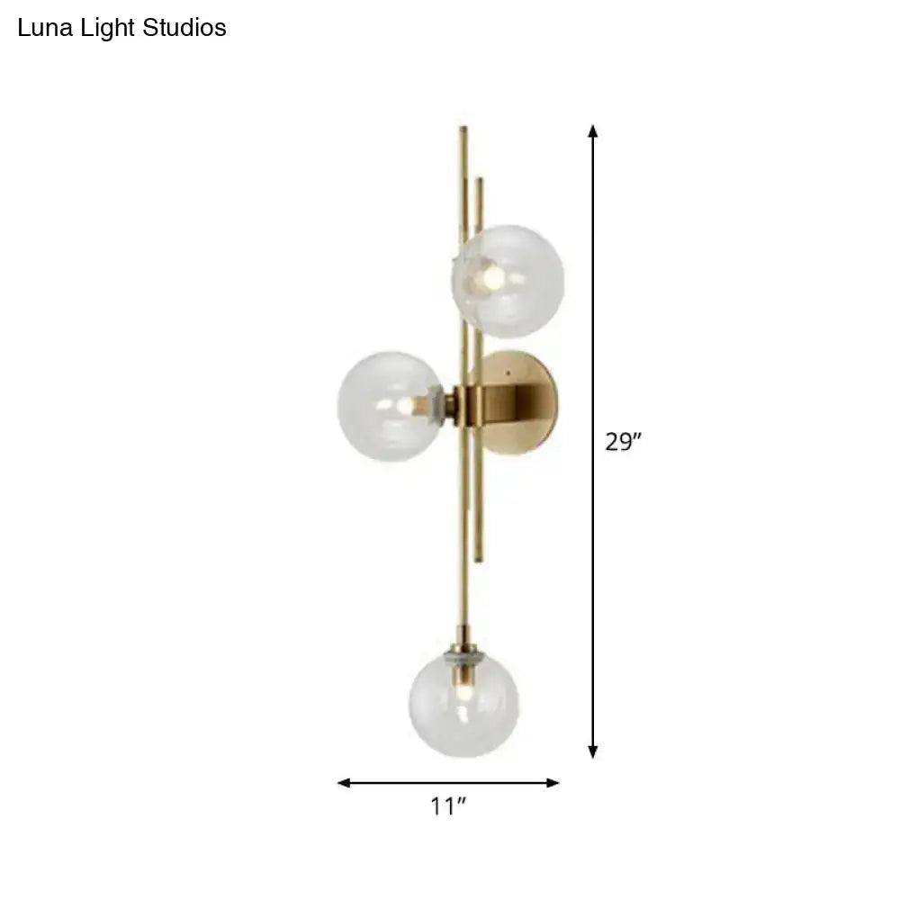 Retro brass wall sconce with three clear glass globes arranged vertically on a gold-toned brass wall fixture for dining room