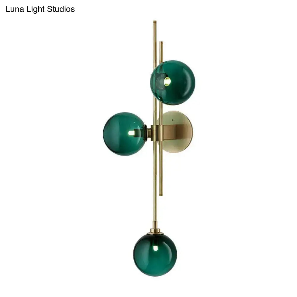 Retro brass wall sconce with three deep emerald green glass spheres on a slender frame for dining room lighting