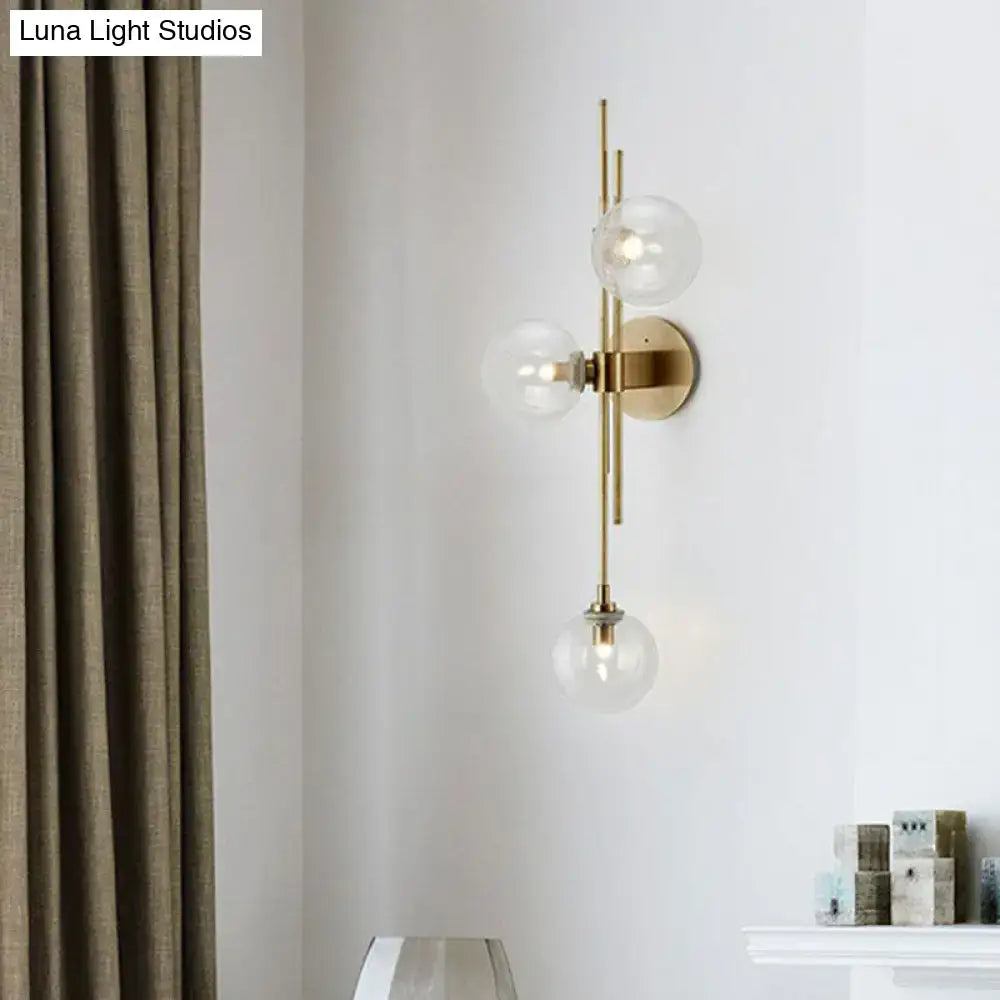 Modern brass wall sconce with three clear glass globe bulbs designed for dining room lighting