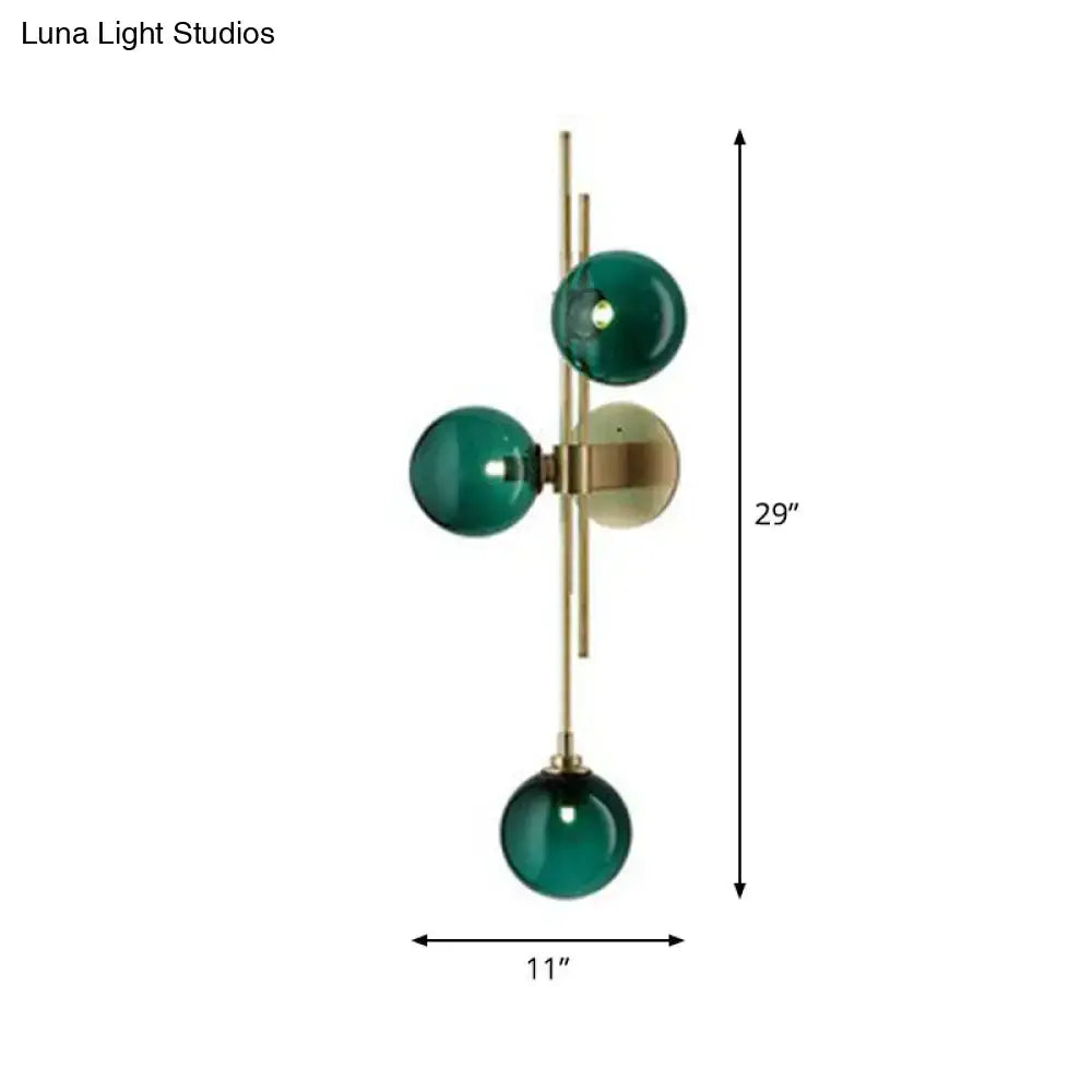 Modern brass wall sconce with three emerald green glass spheres suspended from a slender rod for dining room use