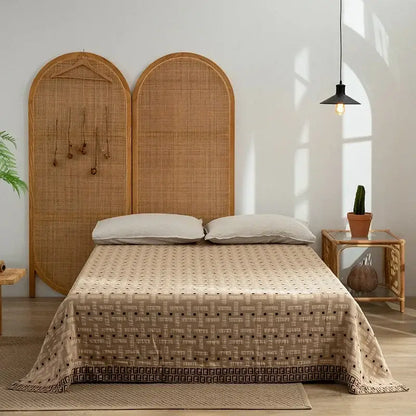Beige decorbites cotton throw blanket with geometric pattern and dark brown border draped over bed with rattan headboards
