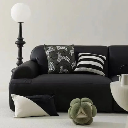 Black leather sofa with two embroidered jacquard luxury pillow covers and a plush green footstool in bedroom setting