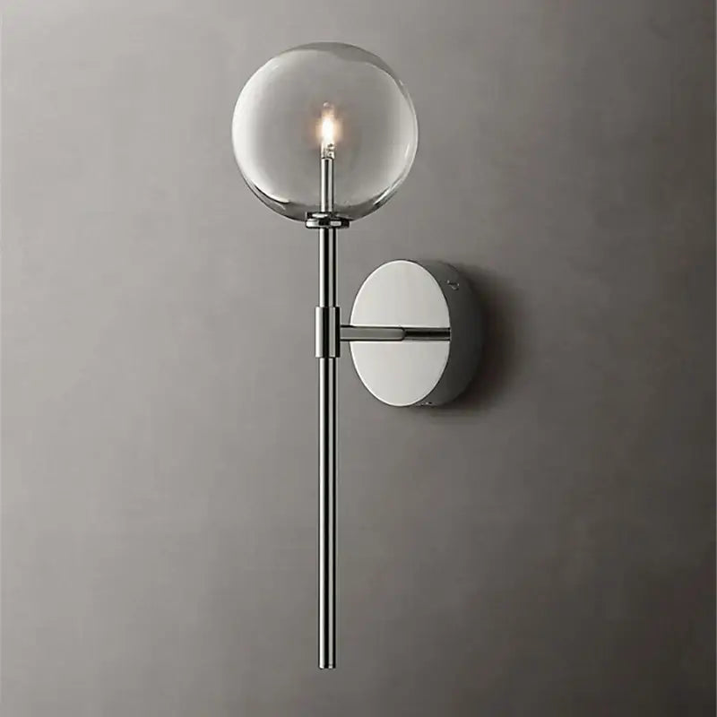Modern wall sconce with a clear glass ball globe, sleek chrome stem, and circular backplate for living room lighting