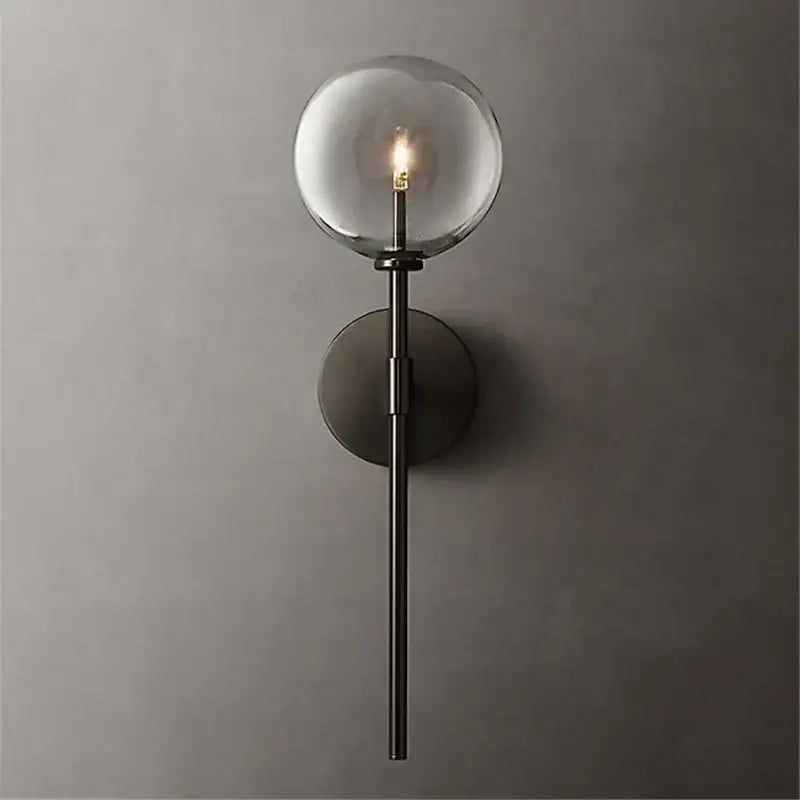 A sleek matte black wall sconce with a clear glass ball globe and illuminated bulb for living room lighting